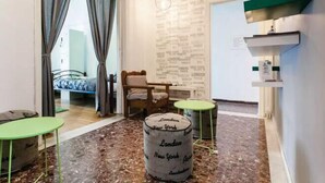 A hotel room with a bed, a chair, a small table, a stool, and a wall with city names. - Athens SmArt Three-Room Apartment (Athens)