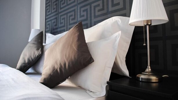 A neatly made bed with white and brown pillows, a black nightstand with a lamp, and a geometric patterned wall. - Athens SmArt Three-Room Apartment (Athens)
