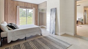 Et soveværelse med seng, ventilator, stort vindue og udsigt til naturen.