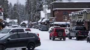 A snowy street with parked cars and buildings.