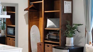 A room with a wooden cabinet, a microwave, wicker baskets, a hanging coat rack, and a chair with a cushion.