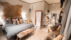 A bedroom with a large bed, a vanity, and a chair.