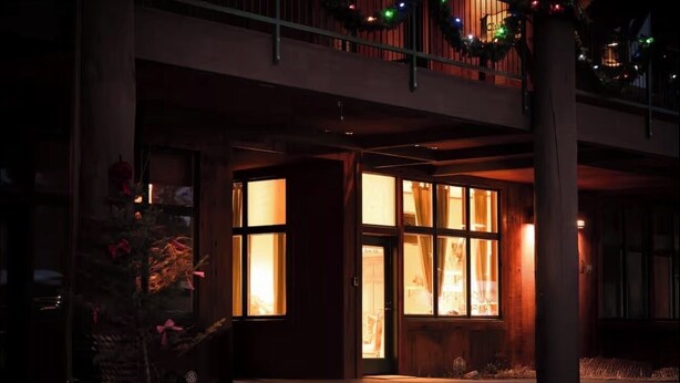 A building with a large entrance, a balcony with railings, and a Christmas tree with lights.