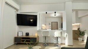 Una sala de estar moderna con un televisor de pantalla plana, un mueble de entretenimiento de madera, dos taburetes blancos y una mesa de centro de vidrio.