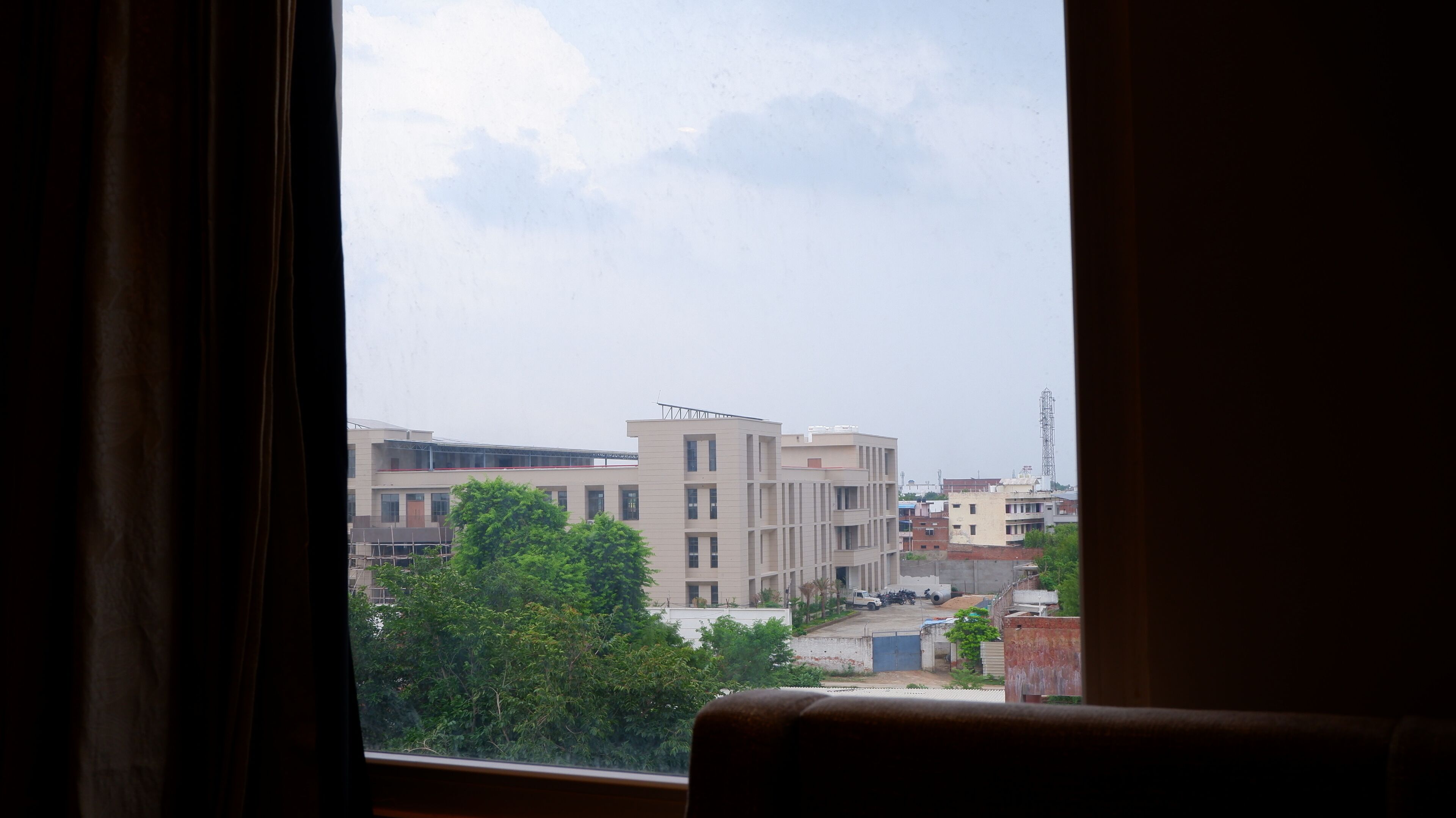 A view through a window with curtains, featuring a multi-story building with a flat roof and a sign on top.