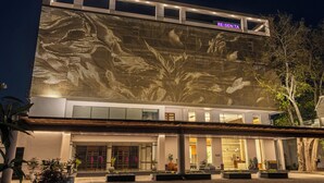Ένα σύγχρονο κτίριο με μια μεγάλη οθόνη LED που προβάλλει ένα σχέδιο με λουλούδια, έναν χώρο υποδοχής με γυάλινες πόρτες και μια καλά φωτισμένη είσοδο.