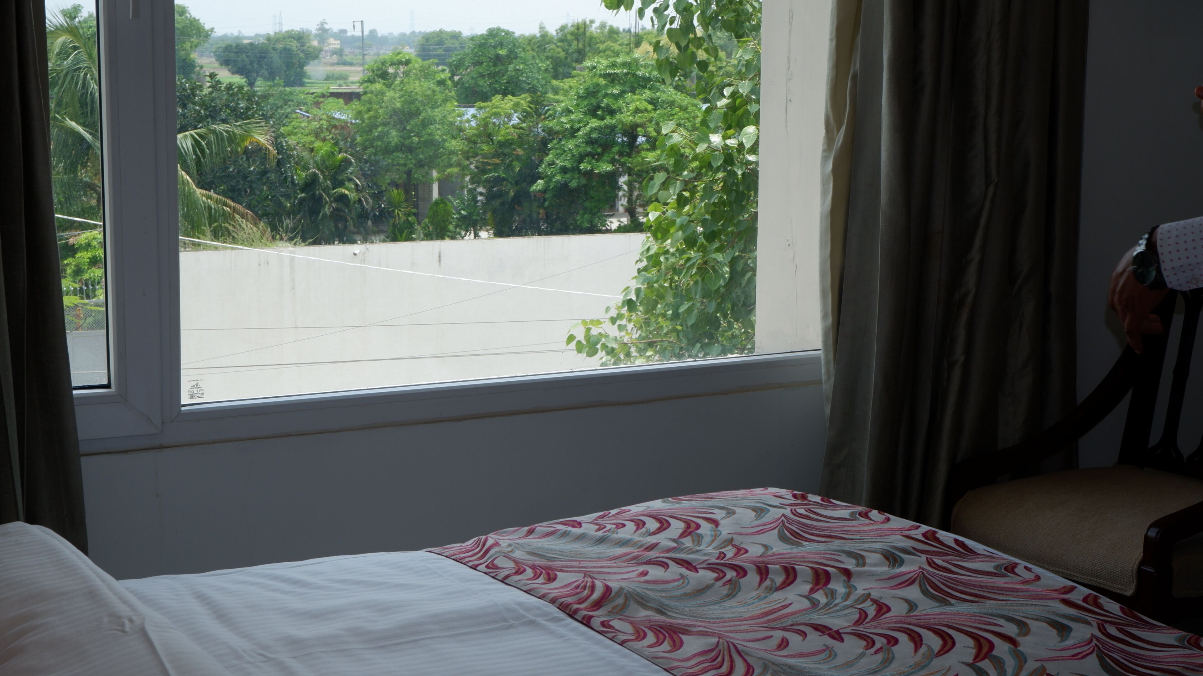 Habitación de hotel con cama, una silla, un ventanal y vistas a zonas verdes y un estacionamiento.