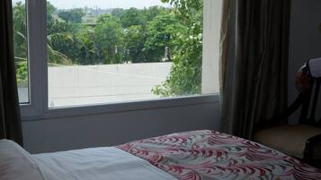 Habitación de hotel con cama, una silla, un ventanal y vistas a zonas verdes y un estacionamiento.