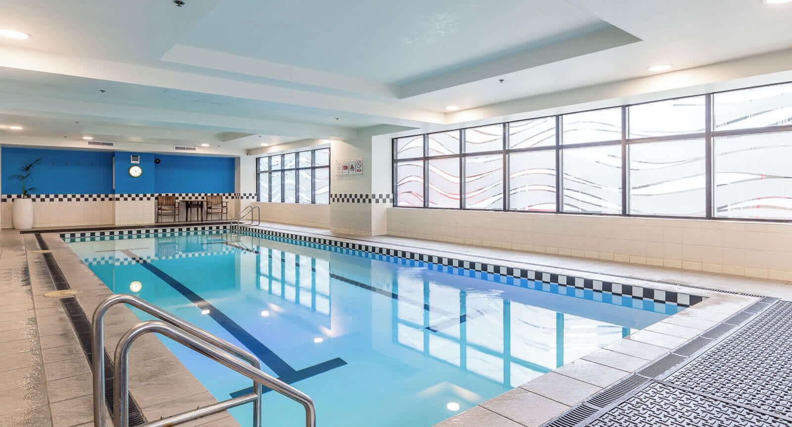 An indoor swimming pool with a checkered border, a clock, and a window with a view of a bridge.