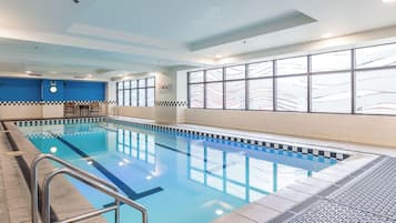 An indoor swimming pool with a checkered border, a clock, and a window with a view of a bridge.