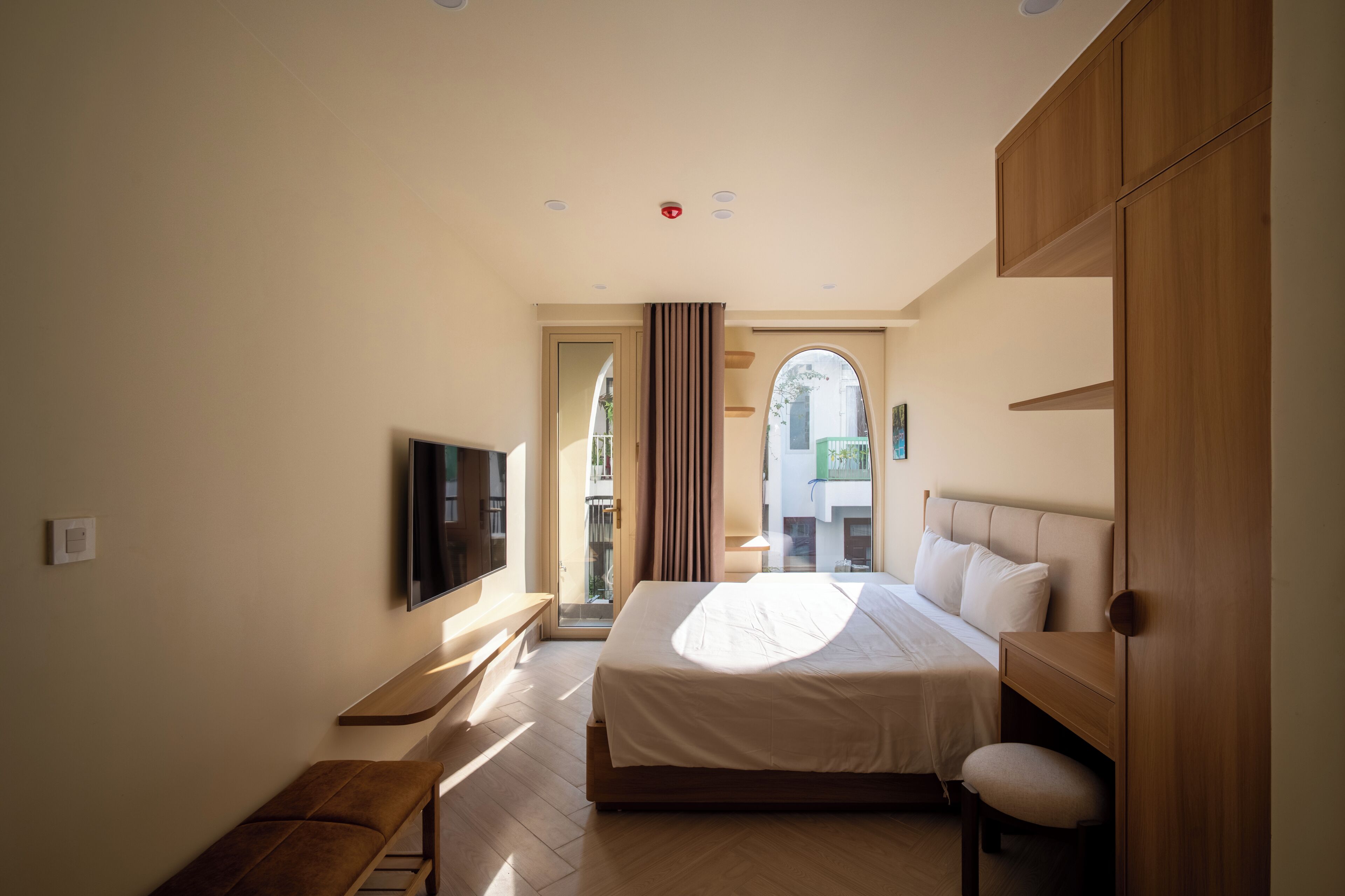 A hotel room with a bed, a TV, a bench, and a view of the outside.