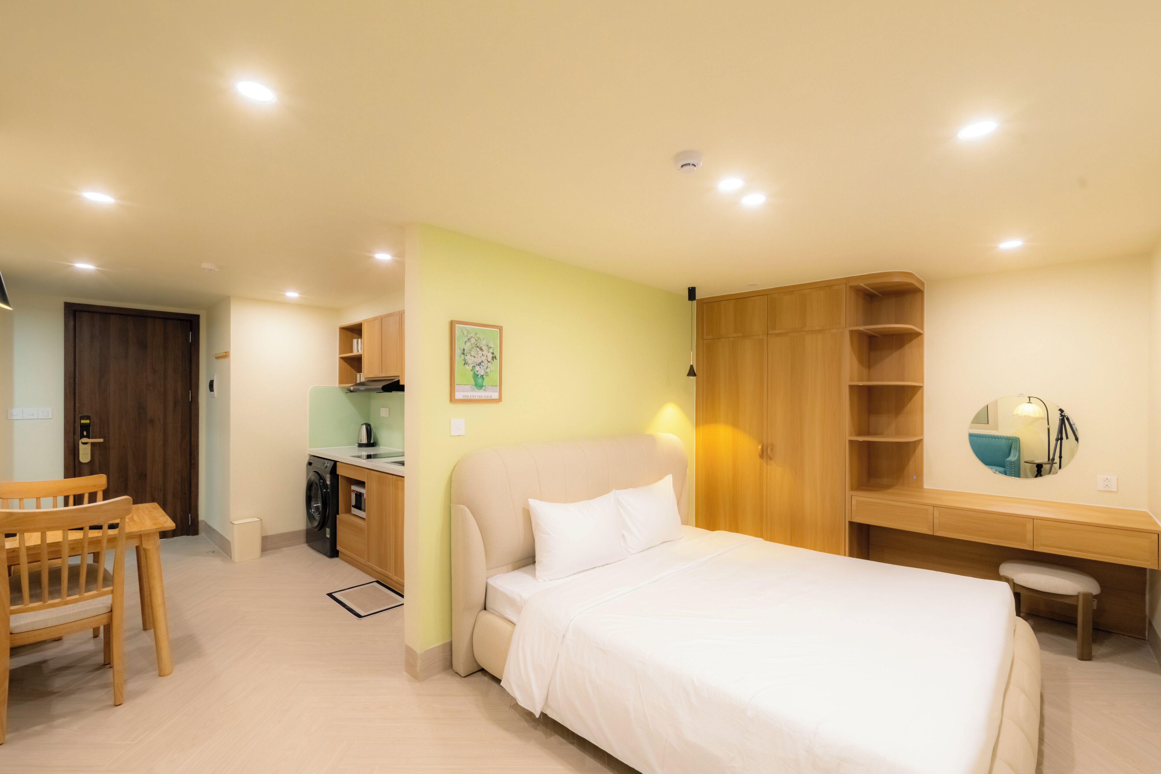 Un dormitorio con cama, escritorio, silla, armario y pequeña cocina.