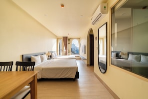Habitación de hotel con dos camas, una mesa de comedor, un ventanal grande con vistas a la ciudad y un equipo de aire acondicionado.
