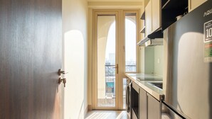 A narrow kitchen with a stainless steel refrigerator, wooden cabinets, and a view through the door. - Weal Apartment (Da Nang)