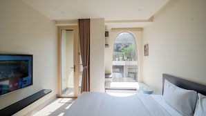 A bedroom with a bed, a TV mounted on the wall, a sliding door leading to a balcony, and a view of the outside. - Weal Apartment (Da Nang)
