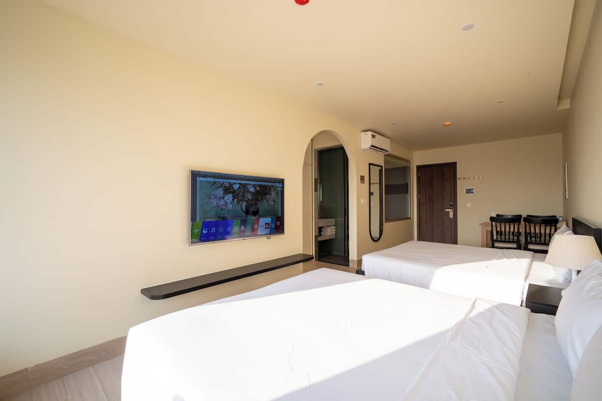 A hotel room with two beds, a TV, a mirror, a desk with a lamp, and a wardrobe.