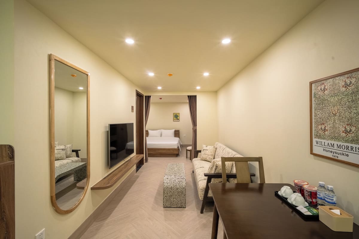 A hotel room with a bed, a sofa, a TV, a wooden table, and a mirror.