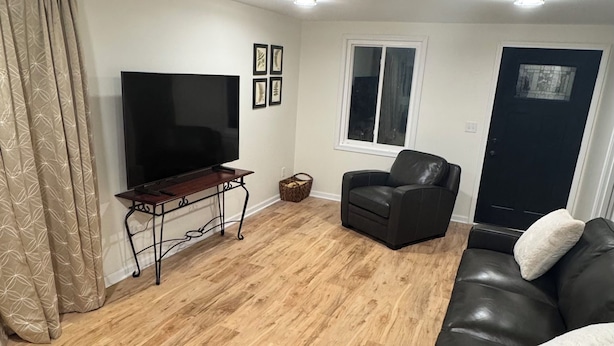 A living room with a flat-screen TV, a leather sofa, a black armchair, a wooden floor, and a door with a window. - Cozy 3-bedroom house in delightful Superiorwith a Riverview (Superior)
