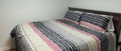 A single bed with a striped bedspread, a wooden headboard, and a circular ceiling light.