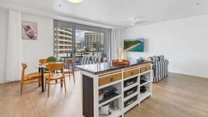 A modern living room with a dining area, a kitchen island, and a large window with a city view. - 403 Harbour Lights (Cairns)