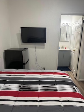 A bedroom with a bed, a TV mounted on the wall, a small desk, and a bathroom visible through an open door. - Serene casita with AC in beautiful Coachella perfect for getaway (Coachella)