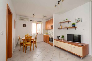 A compact kitchen with a dining area, a TV, and built-in shelves with plants. - Holiday apartment with air conditioning and balcony (Premantura)
