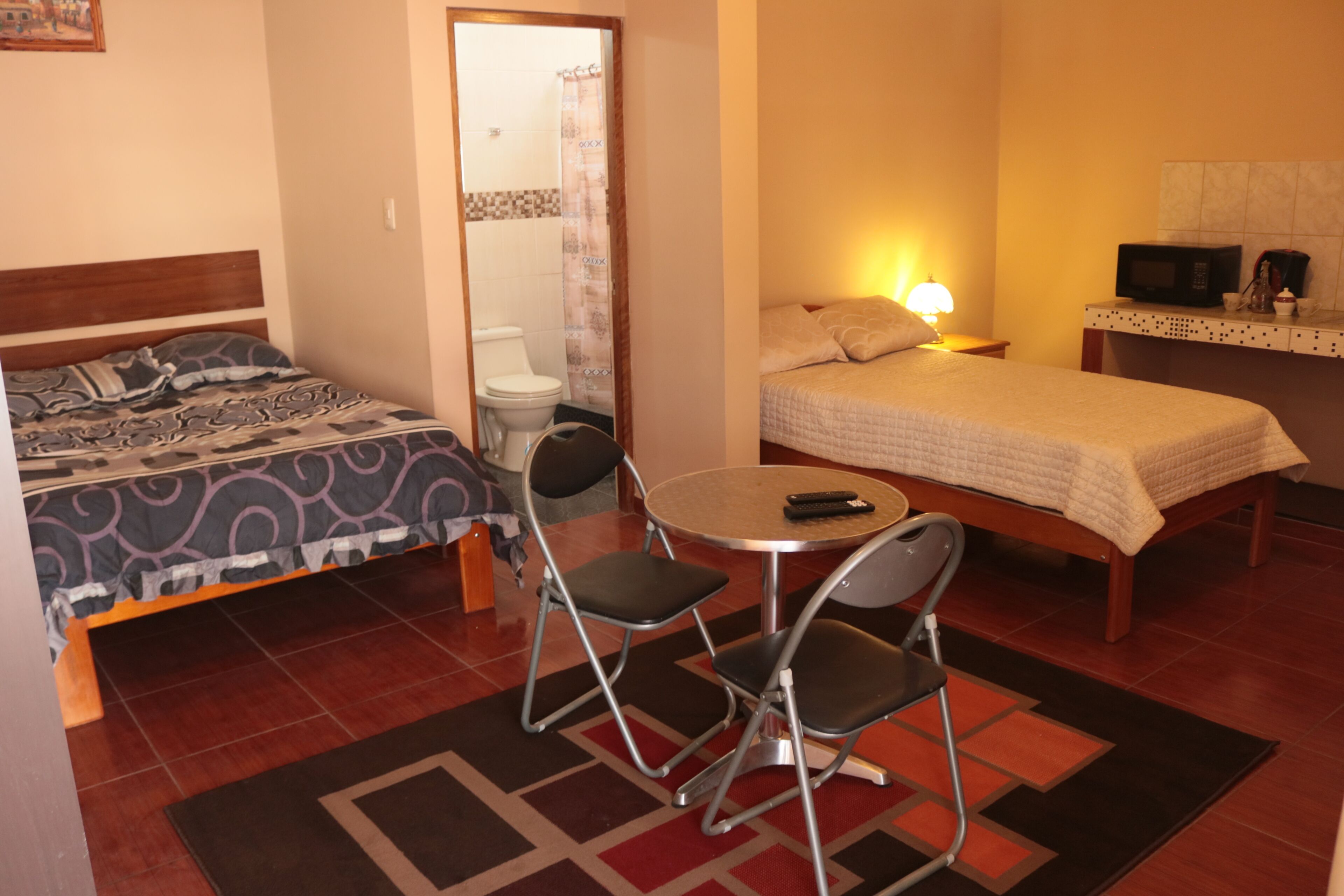 A hotel room with two beds, a round table with chairs, a microwave, and a small table with a lamp.
