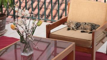 Una silla con cojín, una mesa de vidrio y un jarrón con flores.