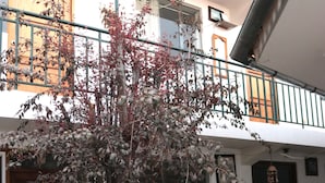 Een binnenplaats met een boom, plantenpotten, een houten deur en een balkon met leuningen.