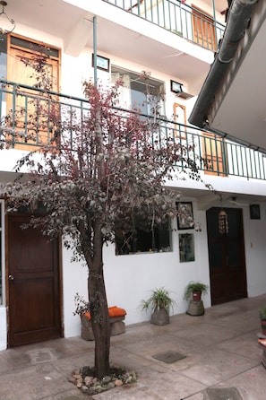 A courtyard with a tree, potted plants, a wooden door, and a balcony with railings. - Lechugal Guest House (Cusco)