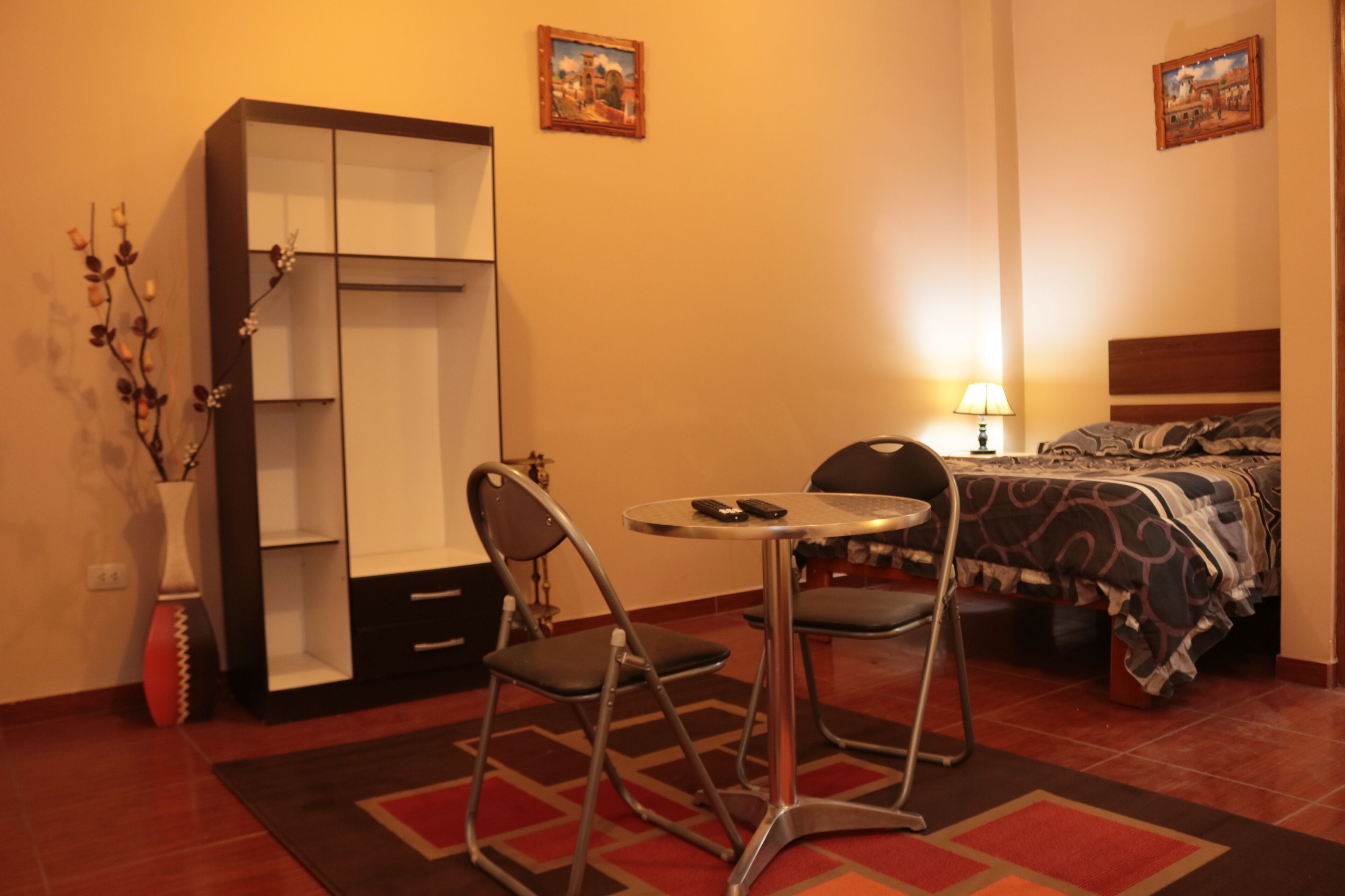 A hotel room with a bed, a desk, a chair, a wardrobe, and a nightstand.