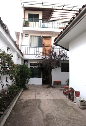 A courtyard with a tree, potted plants, a bench, and a building with a balcony. - Lechugal Guest House (Cusco)