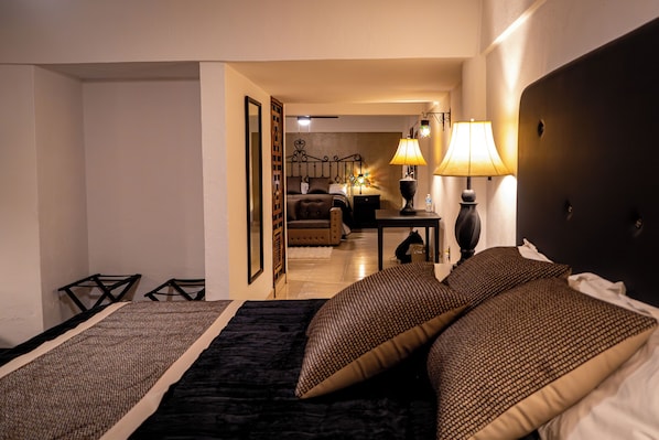 A hotel room with a bed, bedside tables, a lamp, and a view into the adjacent room.