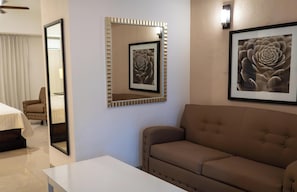 A hotel room with a bed, a sofa, a mirror, and two framed pictures on the wall.