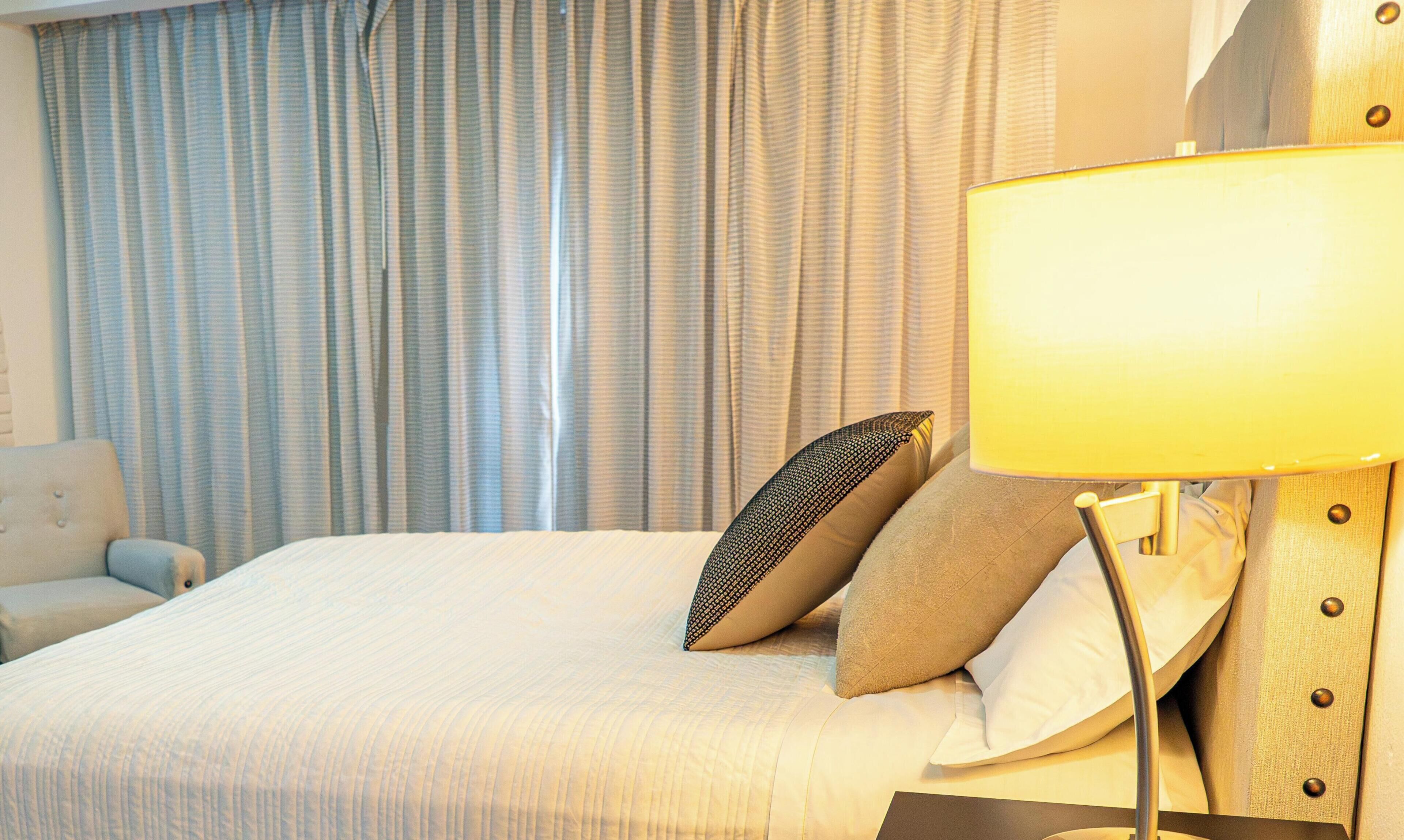 Una habitación de hotel con una cama, una lámpara y cortinas.
