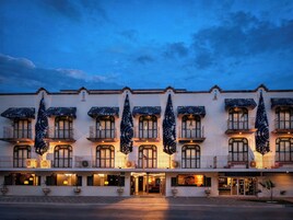 Hotel com várias varandas, plantas em vasos grandes e entrada bem iluminada.