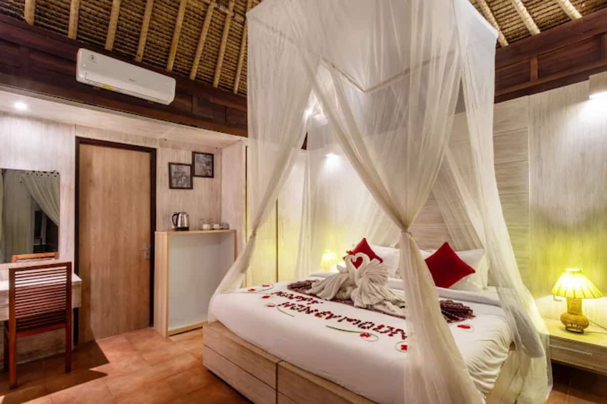 Une chambre à coucher avec un lit à baldaquin, une table de chevet avec une lampe, une chaise en bois et une petite étagère avec une bouilloire.