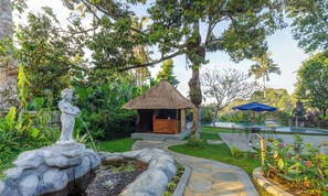 A garden with a statue, a thatched-roof structure, a pond, and a statue by the pool. - Anima Villa Ubud (Payangan)