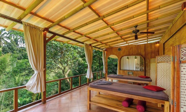 A wooden room with two massage tables, a ceiling fan, and a view of lush greenery. - Anima Villa Ubud (Payangan)