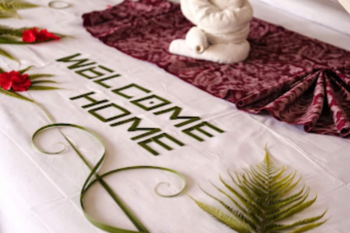 Un lit agrémenté d’une pancarte « BIENVENUE À LA MAISON », d’une sculpture en forme de serviette blanche et de feuilles vertes décoratives.