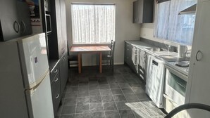 Una cocina compacta con un refrigerador, una mesa de comedor y un ventanal con cortinas.