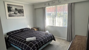 Un dormitorio con una cama, una mesita de noche pequeña, una ventana con cortinas y una obra de arte colgada en la pared.