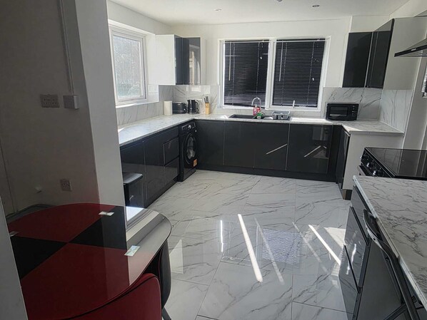 A modern kitchen with black cabinets, a built-in oven, and a large window with blinds.
