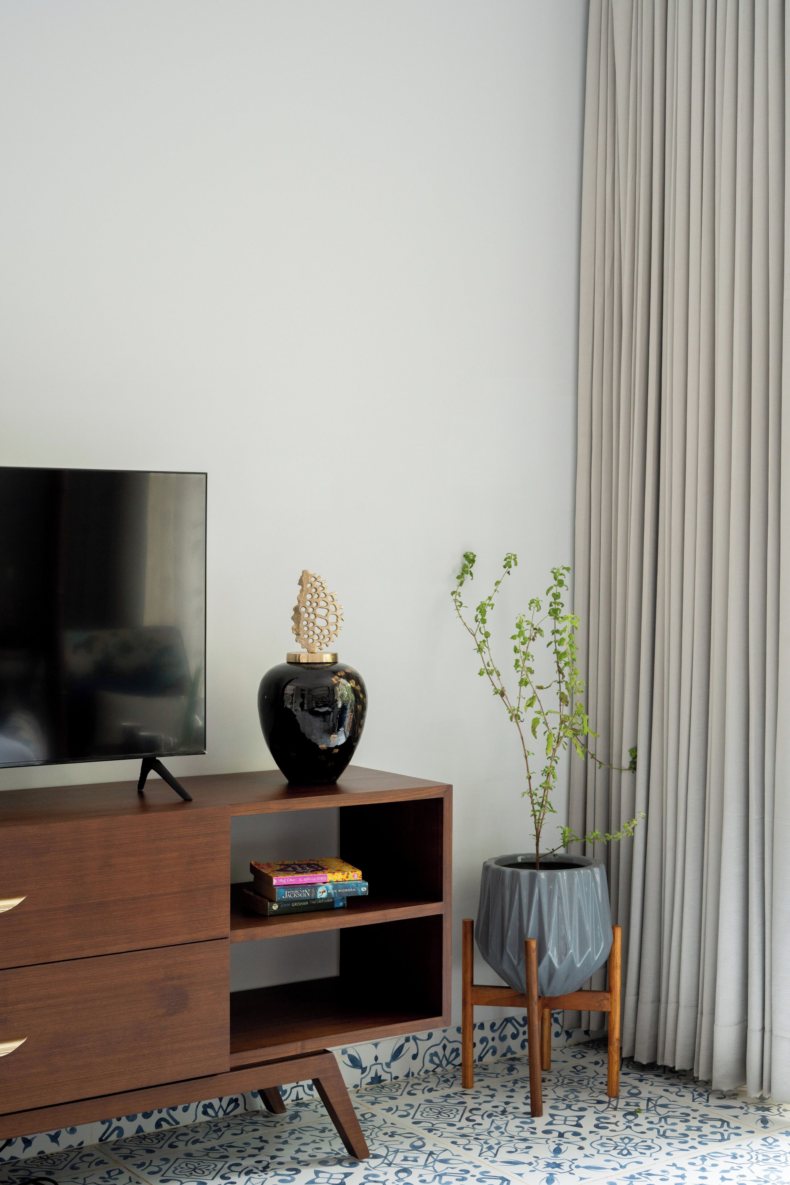 A modern living room with a flat-screen TV, a wooden cabinet, a decorative vase, a potted plant, and a patterned floor.