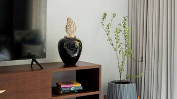 A modern living room with a flat-screen TV, a wooden cabinet, a decorative vase, a potted plant, and a patterned floor.