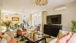 A spacious living room with a sofa, coffee table, and a television. There is a staircase leading to another level, and a large window providing natural light. - ELIVAAS Prive Suntuarios Ikkebana 4 BHK  (Assagao)