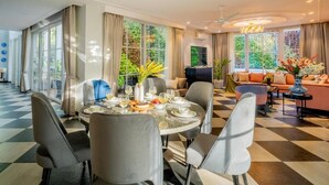 A dining area with a round table set for four, surrounded by chairs, and a living area with a sofa and a TV. - ELIVAAS Prive Suntuarios Ikkebana 4 BHK  (Assagao)