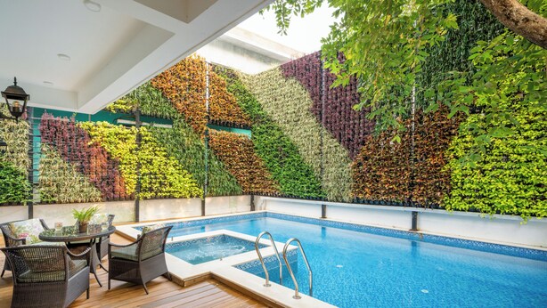 A swimming pool with a wooden deck and outdoor furniture, surrounded by a wall of various plants. - ELIVAAS Prive Suntuarios Ikkebana 4 BHK  (Assagao)