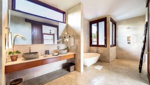 A modern bathroom with a large mirror, a stone sink, a freestanding bathtub, and a shower area. - Casa Brio Bali (Seminyak)