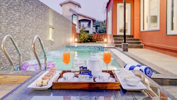 Bandeja de desayuno con pasteles, café y jugo junto a una piscina, con un muro de piedra y un edificio al fondo.